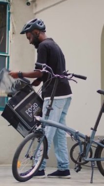 Dikey video: Erkek teslimat çalışanı kadın kadına fast food siparişi veren, ön kapıda ofis yemeği dağıtım hizmeti veren. Kuryeden restoran siparişi alan kadın, yemek hazırlayan müşteri.