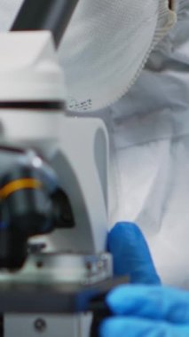 Dikey video: Ekipmanlı laboratuarda mikroskop üzerinde çalışan deneyimli biyolog. Aşı evrimini inceleyen kimyagerler yüksek teknolojili araştırma tanıları kullanıyorlar.