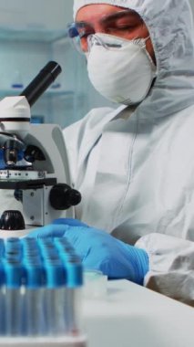 Dikey video: Biyoloji bilimadamı mikroskop kullanarak ilaç laboratuarında yeni aşı araştırması yapıyor. Yüksek teknoloji araştırma teşhisi kullanarak virüs evrimini inceleyen iş arkadaşları