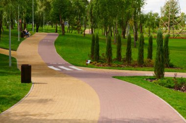 Renkli kırmızı ve sarı tuğlalı taş yollar yeşillikler arasında bisiklet işaretleri, çevre tasarımı bitkilerle kentsel peyzaj, güneşli bir yaz gününde park
