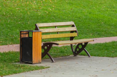 Manzaralı bir parkta, eğlence yolu boyunca çöp tenekesi olan ahşap koltuk.