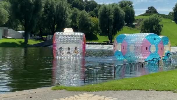 2021年7月25日ドイツ バイエルン州ミュンヘン オリンピック公園 子供向けのエンターテイメント 遊園地の乗り物 浮遊プラスチック製の水ウォーキングバレル 子供たちがズボンと — ストック動画