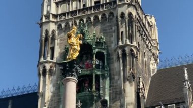 Münih, Almanya. Marienplatz 'da (Mary' nin meydanı) New City Hall (Neues Rathaus) önünde ünlü Marian Sütunu. Carillon (Glockenspiel) müzik. Güneşli bir günde sesli video. 4K