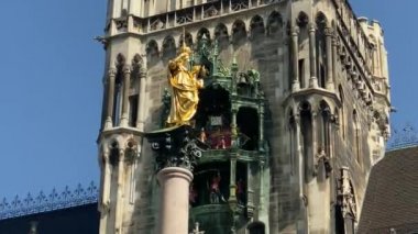 Münih, Almanya. Marienplatz 'da (Mary' nin meydanı) New City Hall (Neues Rathaus) önünde ünlü Marian Sütunu. Carillon (Glockenspiel) müzik. Güneşli bir günde sesli video. 4K