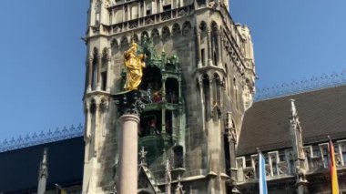 Münih, Almanya. Marienplatz 'da (Mary' nin meydanı) New City Hall (Neues Rathaus) önünde ünlü Marian Sütunu. Carillon (Glockenspiel) müzik. Güneşli bir günde sesli video. 4K