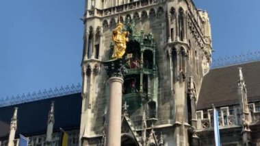 Münih, Almanya. Marienplatz 'da (Mary' nin meydanı) New City Hall (Neues Rathaus) önünde ünlü Marian Sütunu. Carillon (Glockenspiel) müzik. Güneşli bir günde sesli video. 4K