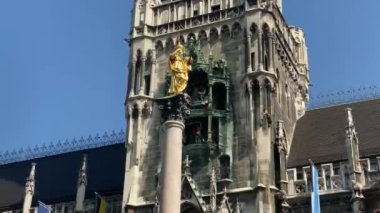Münih, Almanya. Marienplatz 'da (Mary' nin meydanı) New City Hall (Neues Rathaus) önünde ünlü Marian Sütunu. Carillon (Glockenspiel) müzik. Güneşli bir günde sesli video. 4K