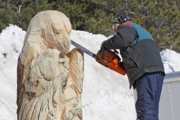 Mann schnitzt Gesicht mit Kettensäge auf riesigen Bären aus Baumstamm — Stockfoto