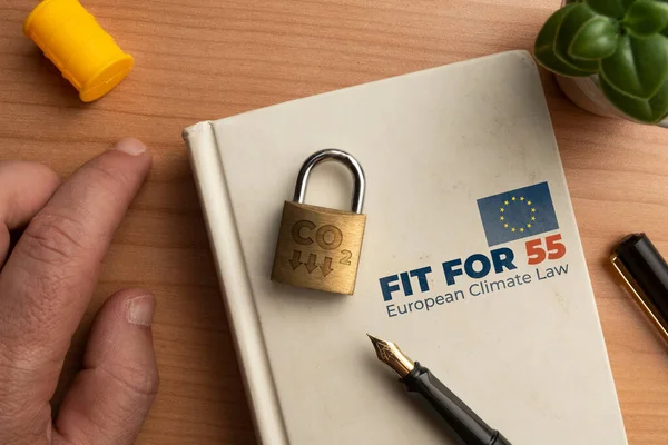 Fit for 55 european climate law concept: a book on a wooden table with a man hand a lock and a pen