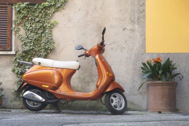 Carrara, Italy - July 10, 2022 - Modern orange Vespa Piaggio parked in an Italian alley