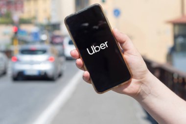 Carrara, Italy - July 13, 2022 - Woman holds a smartphone on a background of cars showing the Uber log