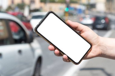 Woman holds a smartphone with blank screen on background with busy street near a traffic light