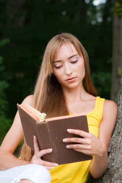 Fiatal nő ül a fán, és egy könyvet olvas — Stock Fotó