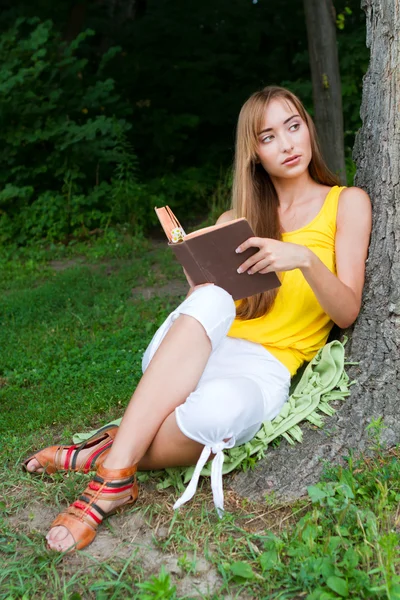 Mujer joven sentada cerca del árbol y leyendo un libro —  Fotos de Stock