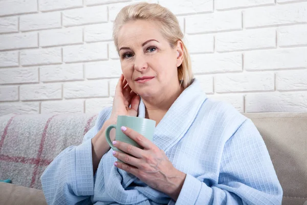 Glücklich schöne Frau mittleren Alters trinkt Kaffee auf dem Sofa zu Hause — Stockfoto