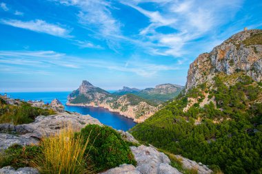 Koyun kayalık kıyıları, bir uçurum, beyaz bulutlu mavi gökyüzü ve güneş.