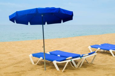 Boş güneş akciğerleri ve şemsiye kötü hava gününde plaj hattında.,