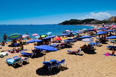 LLORET DE MAR, İSPAN - 29 Temmuz 2019: Şemsiyeler ve güneş sıcak bir günde sahilde akın eder, Costa Brava. Plaj istirahatı kavramı. Yaz seyahati.