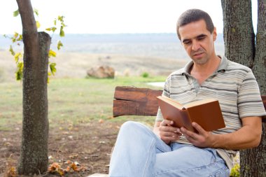 bahçede bir kitap tadını çıkarıyor adam