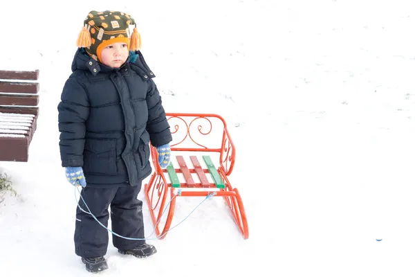 Giovane ragazzo che gioca con una slitta nella neve — Foto Stock