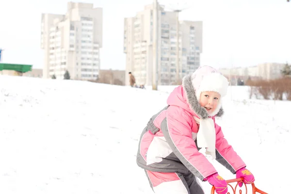 Söt liten flicka som leker med en släde i snö — Stockfoto