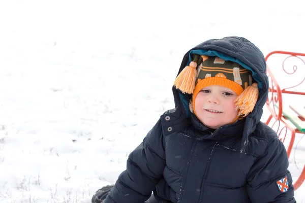 Malý chlapec sedí s jeho saně ve sněhu — Stock fotografie