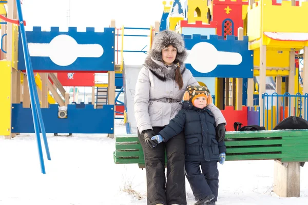 Moeder en zoon in een besneeuwde kinderspeelplaats — Stockfoto