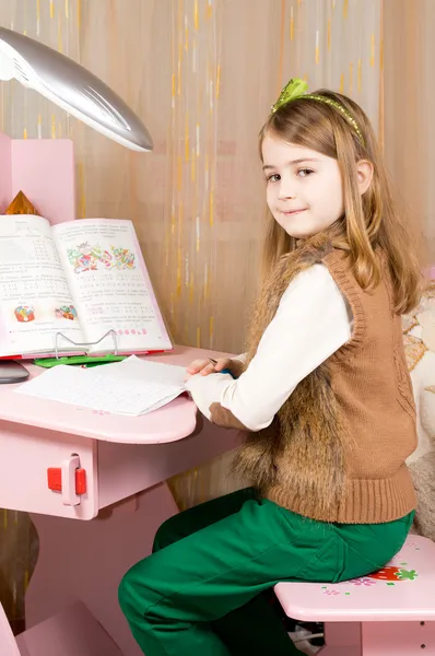 Усміхнена молода дівчина працює за її столом — стокове фото