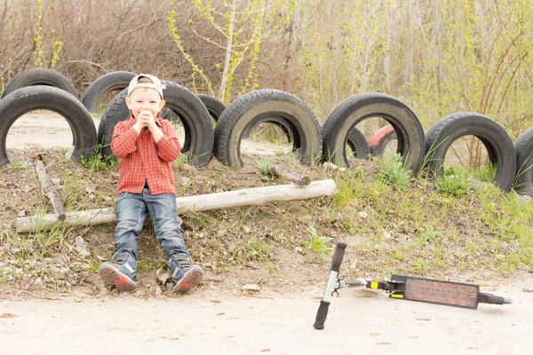 Kleiner Junge spielt mit seinem Roller in einem Park — Stockfoto