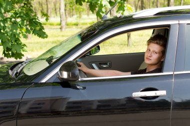 schattige jonge jongen een zwarte auto rijden en poseren