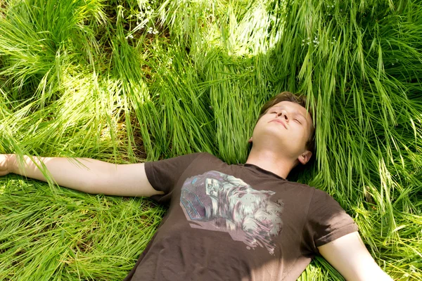 Mladý muž spí v dlouhé zelené trávě — Stock fotografie