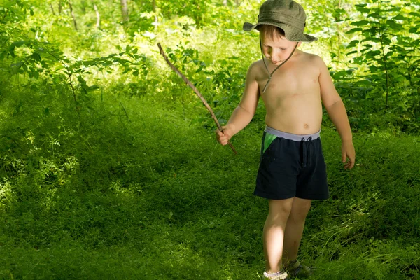 Piccolo ragazzo che gioca nel bosco con un bastone — Foto Stock