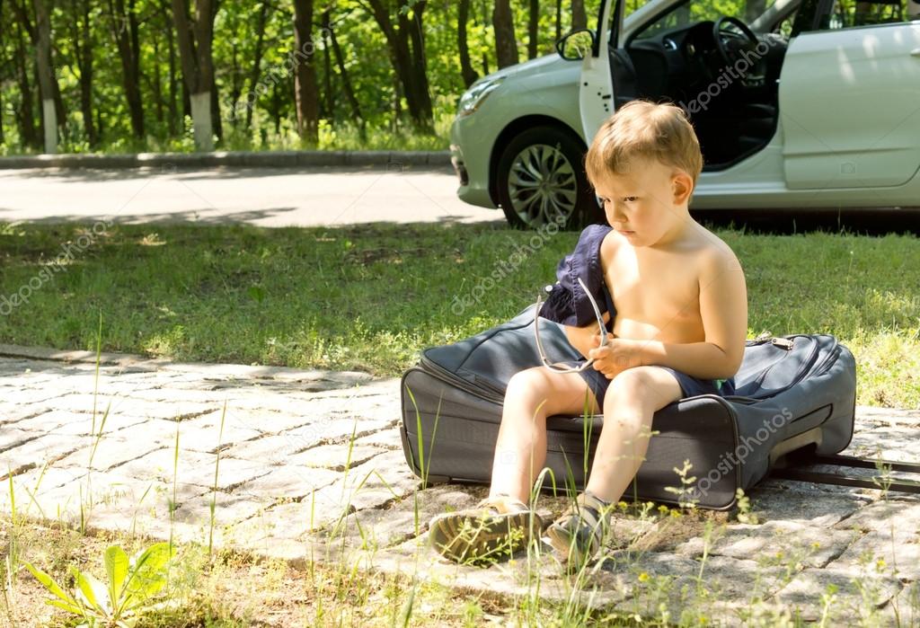 Young boy sitting on a travel bag on the roadside