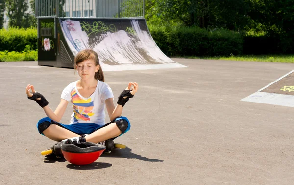 Дівчина в роликових лопатях сидить медитуючи — стокове фото