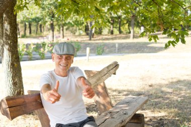 Beyaz adam başparmak yukarıya bir bankta oturan gösterilen
