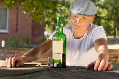 Melancholic drunk man looking at a bottle of wine clipart