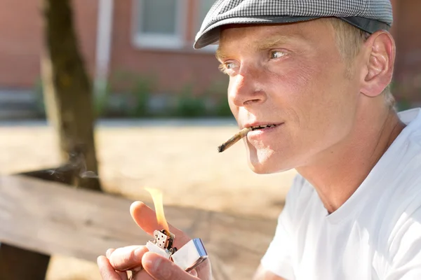 Positive thoughtful man lighting a brown cigarette — Stock Photo, Image