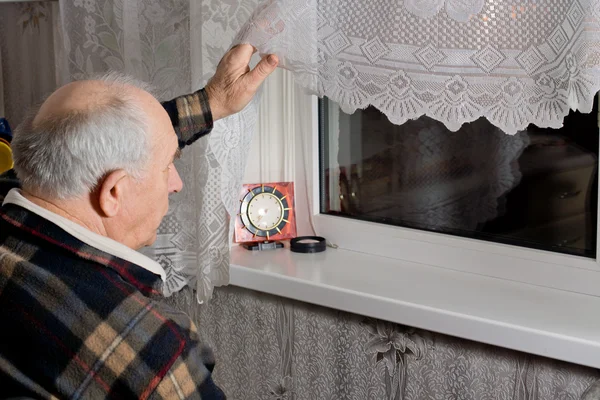 Oudere man peering uit door het venster — Stockfoto