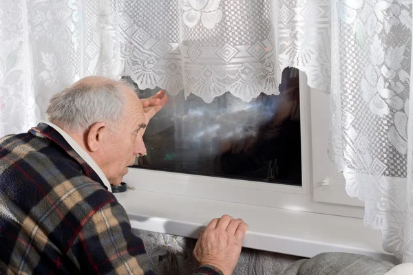 Hombre mayor mirando por una ventana por la noche — Foto de Stock