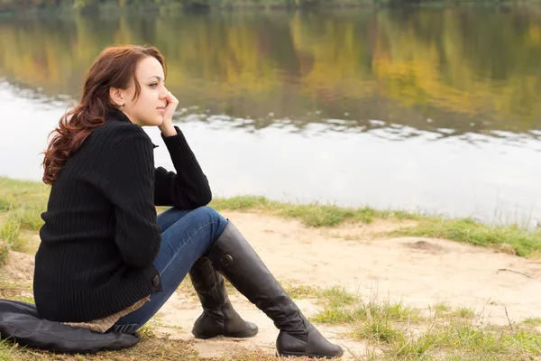 Jeune femme branchée assise sur une rive de rivière — Photo