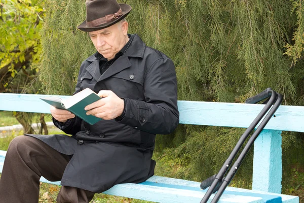 Elderly disabled man sitting outdoors reading — Stock Photo, Image