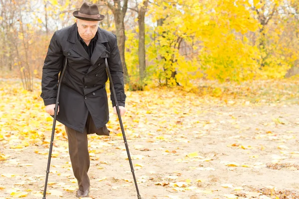 Elderly disabled man on crutches in a park — Stock Photo, Image