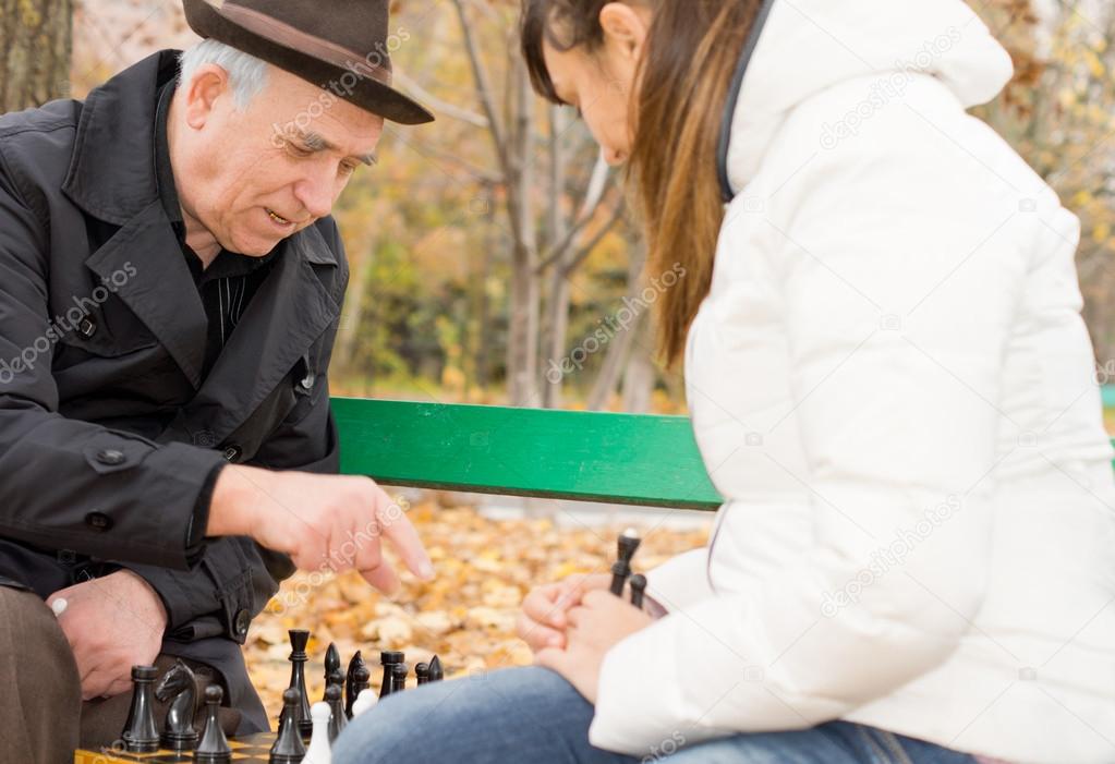 Senior man playing chess with his granddaughter