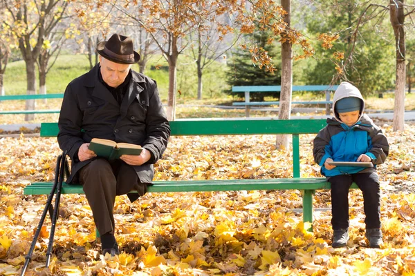Homem idoso e menino pequeno sentado em um banco de parque — Fotografia de Stock