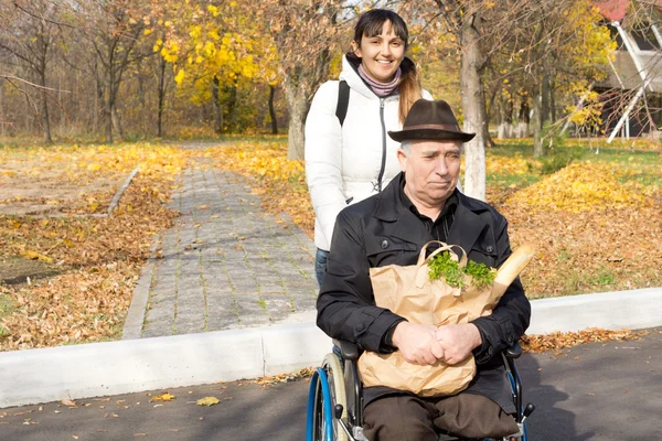 Pomocne kobieta pchanie starszy człowiek na wózku inwalidzkim — Zdjęcie stockowe
