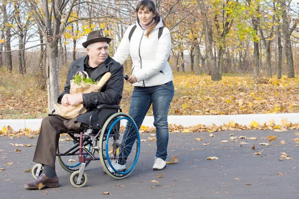 Woman helping a disabled pensioner in a wheelchair — Stock Photo, Image