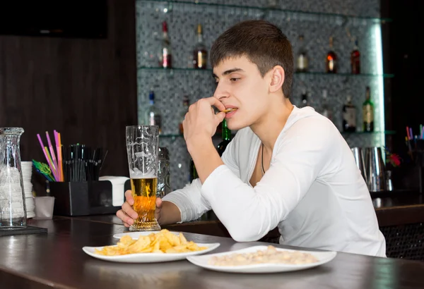 Oturan genç adam içiyor ve bir barda yemek — Stok fotoğraf