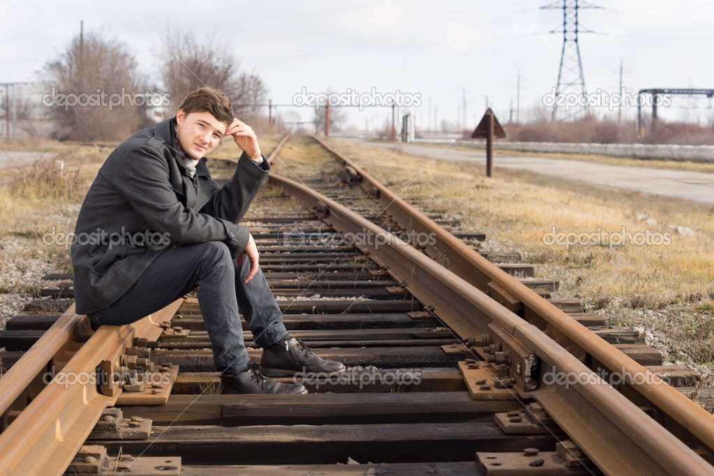若い男が 金属鉄道の線路の上に座っています ストック写真 C Vaicheslav