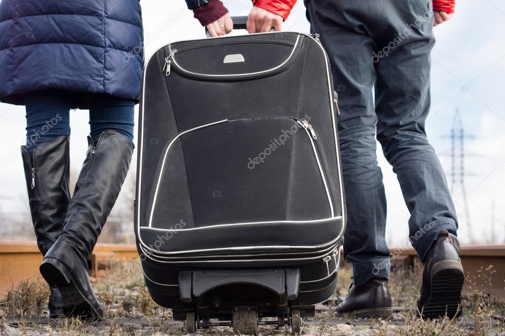 Couple pulling a suitcase along a stony path