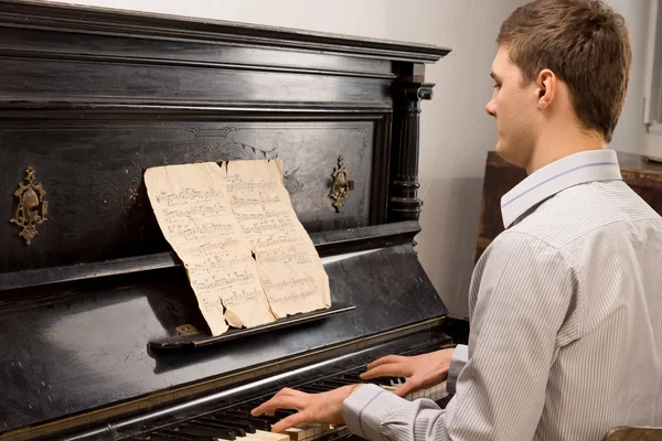 Jonge man afspelen van muziek op een houten piano — Stockfoto